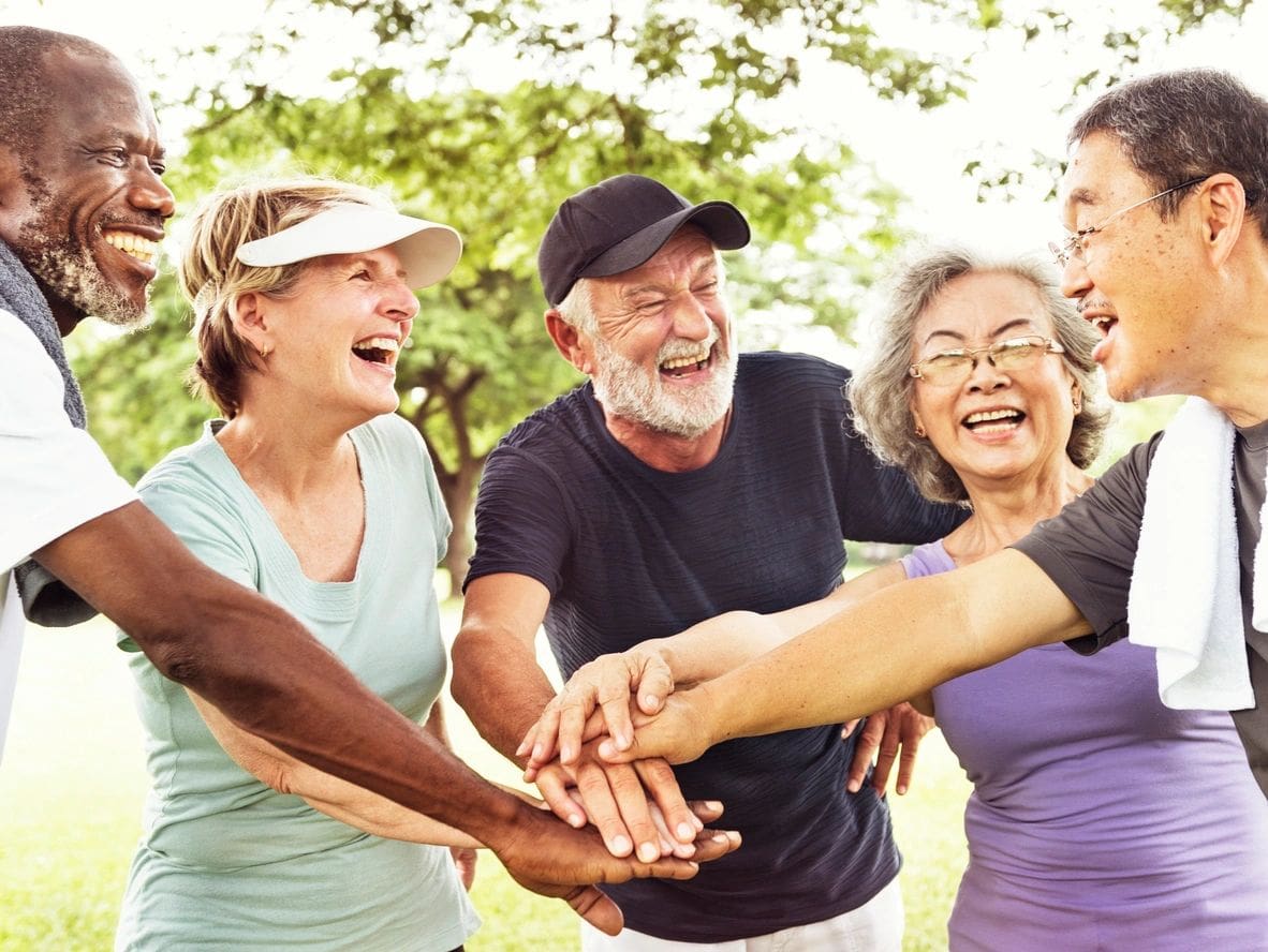 A group of seniors happily joining hands outdoors.