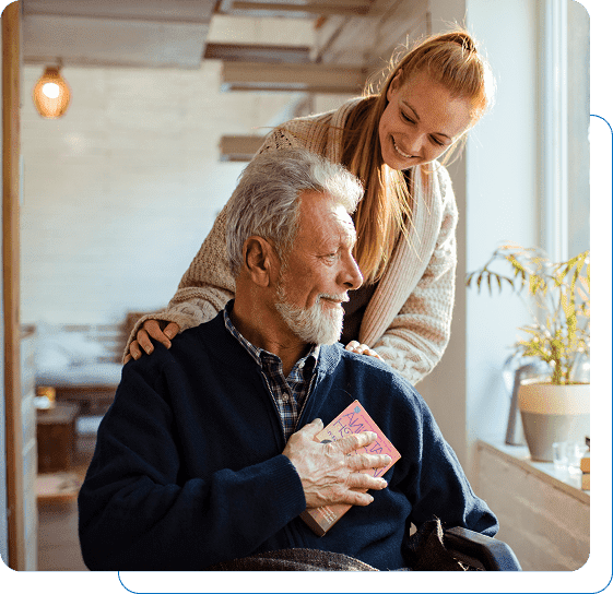 A young woman lovingly embraces an elderly man holding a gift.
